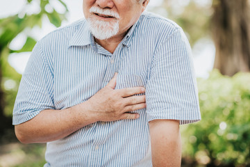 Cropped shot of senior man holding his chest and feeling pain suffering from heart attack outdoor...