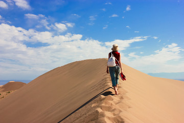 Tourist girl walking to the top of the Singing Sand Dunes in Kazakhstan