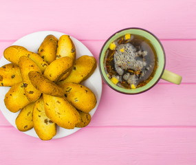 Rusks on a white plate and a cup of tea on a wooden pink background.