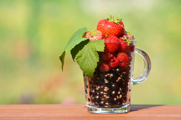 Freshly washed berries (currant, raspberry) in a transparent glass.