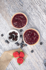 Vertical image of two fruit tarts with blackberries and blueberries on a wooden background 