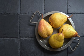 Dojrzałe gruszki na zabytkowej tacy, na czarnym kamieniu łupkowym, tło