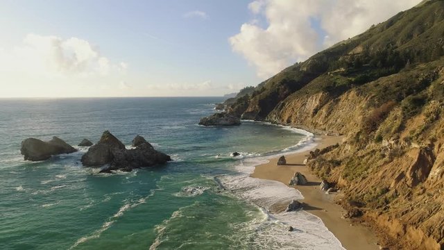 Aerial shot flying over a pristine sandy beach on a rugged coastline. Very colorful and epic views. Rocks sticking out of the ocean.