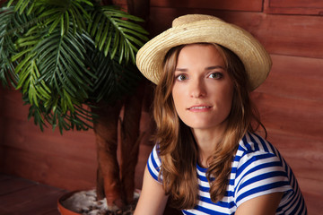 Beautiful woman in a striped shirt and a hat sitting on the veranda of a summer country house