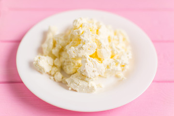 Cottage cheese on a white plate on a pink wooden background.