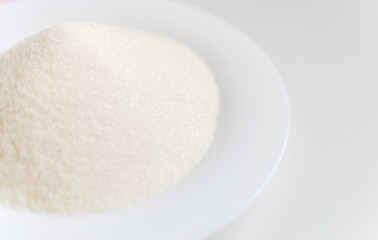 Fototapeta na wymiar Sugar on a white plate on a white background.