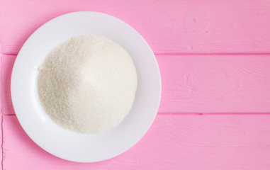 Sugar on a white plate on a wooden pink background.