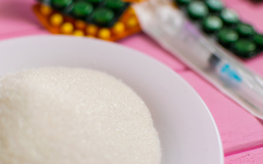 Sugar on a plate, syringe and pills on a pink background. The concept of possible harm from sugar.