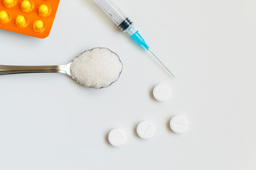 A spoon of sugar, a syringe and pills on a white background. The concept of harm to sugar and the onset of diabetes.
