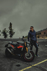 Rider stand on a mountain next to motorcycle and looks as
