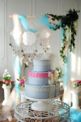 Свадебный торт возле свадебной арки с ловцами снов и колонами в белом интерьере с камином
