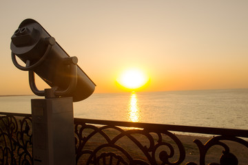 Binoculars on the coast of the sea. Tourist telescope on a background of sunset on the waterfront....