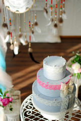 Свадебный торт возле свадебной арки с ловцами снов и колонами в белом интерьере с камином