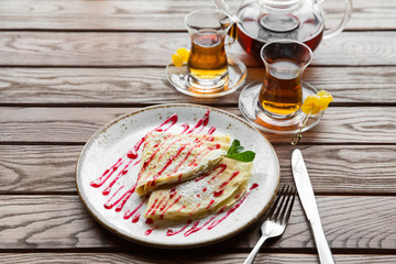 Delicious thin pancakes served with strawberry sauce on a wooden rustic table