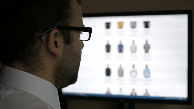 A man looks at the goods in the online clothing store, sitting at the desk. Computer online shopping . PC monitor showing blur feed page .