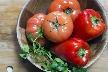 tomato and red sweet paprika, with greens leaves in a wooden bowl on a wooden board,  flat lay..