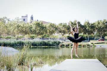 Classical ballerina jumping on a footbridge of an urban lake on a sunny day