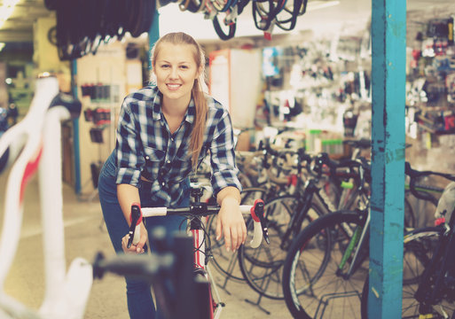 Portrait of girl who is standing with bicycle in store.