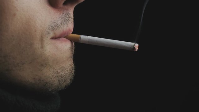 Close up of a brutal man smoking a cigarette at black background.