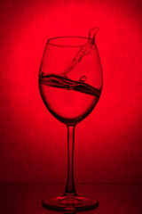 Splash of water in a wine glass on a red background