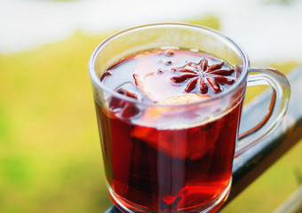 Hot red mulled wine with oranges, cinnamon and anise stars in glass cup on a hand railing of balcony