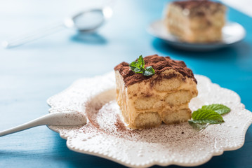 Italian tiramisu dessert on a porcelain plate, on a blue background