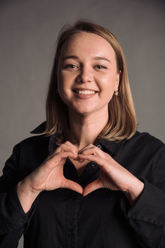 portrait of smiling young woman in black shirt isolated on gray studio background posing to the camera, hands like a heart