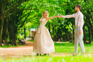 The girl in a beautiful long dress holds her boyfriend for a hand and leads his in a green park