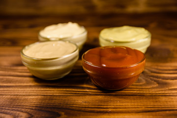 Different sauces in glass bowls on wooden table