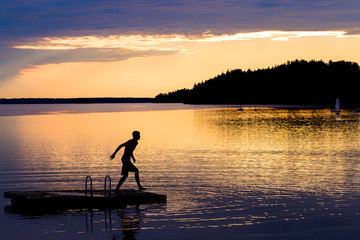 Silhouette of young man jumping from a pontoon into lake at sunset