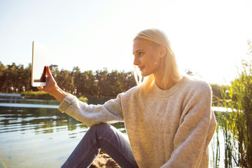 girl in an autumn park near a lake holds a tablet