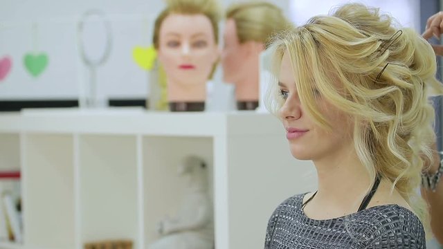 Cute blonde girl admires herself in the mirror in the beauty salon and smiles. Close up