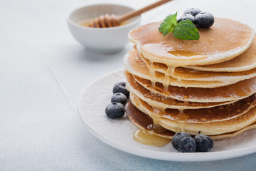 A stack of delicious pancakes with honey and blueberries on a light blue background. with copy space