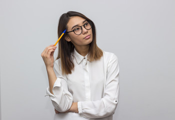 Indoor portrait of beautiful brunette asian woman with pencil and glasses having a lot of questions. Young student or businesswoman concept. Selective focus and shallow DOF