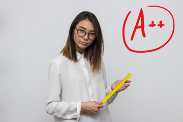 Young and funny strict teacher with glasses shakes ruler in hands on the grey background with good mark symbol. School or university concept. Selective focus and shallow DOF