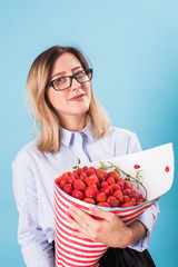 Bouquet of strawberries in the hands of a girl on blue background