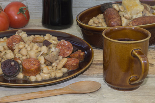 Un plato con  alubias cocinadas, con chorizo y morcilla, una jarra con vino 