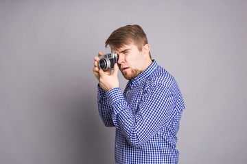 Young photographer man holding retro camera on a gray background