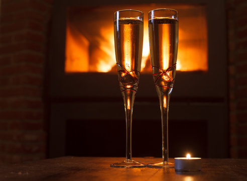 Two glasses of champagne in front of log fire with candle