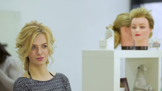 Cute blonde girl admires herself in the mirror in the beauty salon. Close up