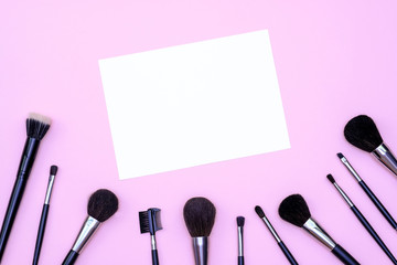 Obraz na płótnie Canvas Set of makeup brushes on pink colored composed background. Top view point, flat lay, space for text on note.