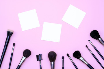 Obraz na płótnie Canvas Set of makeup brushes on pink colored composed background. Top view point, flat lay, space for text on note.