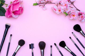 Obraz na płótnie Canvas Set of makeup brushes, decorative cosmetics and flowers on pink colored composed background. Top view point, flat lay, space for text