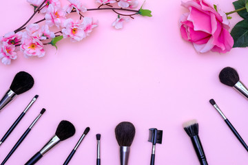 Obraz na płótnie Canvas Set of makeup brushes, decorative cosmetics and flowers on pink colored composed background. Top view point, flat lay, space for text