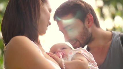 Young happy parents in love, father kissing sleeping baby child in summer park. Slow motion.