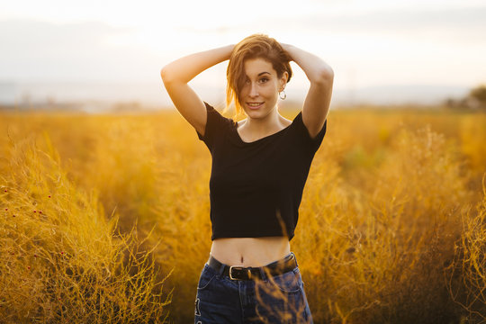 Young beautiful girl in the field. She wears a black T-shirt and jeans. Yellow background.