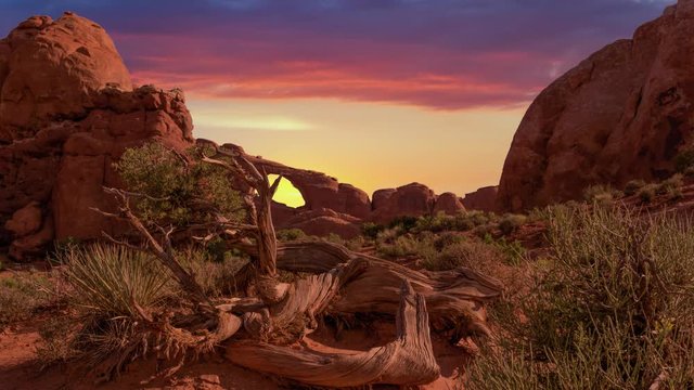 Golden sunset is animated in a time lapse effect beyond a natural arch in the desert landscape