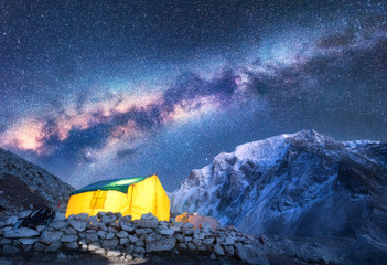 Milky Way, yellow glowing tent and mountains. Amazing scene with himalayan mountains, starry sky at...
