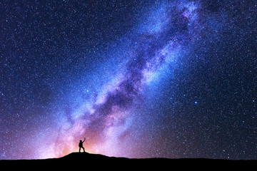 Silhouette of happy woman with trekking poles against purple Milky Way at night. Space background. Landscape with girl on the mountain, bright milky way, sky with stars. Galaxy. Travel. Starry sky
