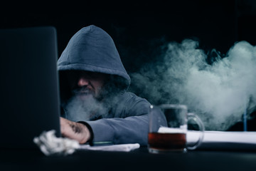 male hacker sitting at a table and smoking